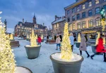 People walk through a snowy square in Old Montreal with bright lights and old buildings all around