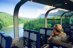 A man looks out the panoramic windows as a train goes through the mountains