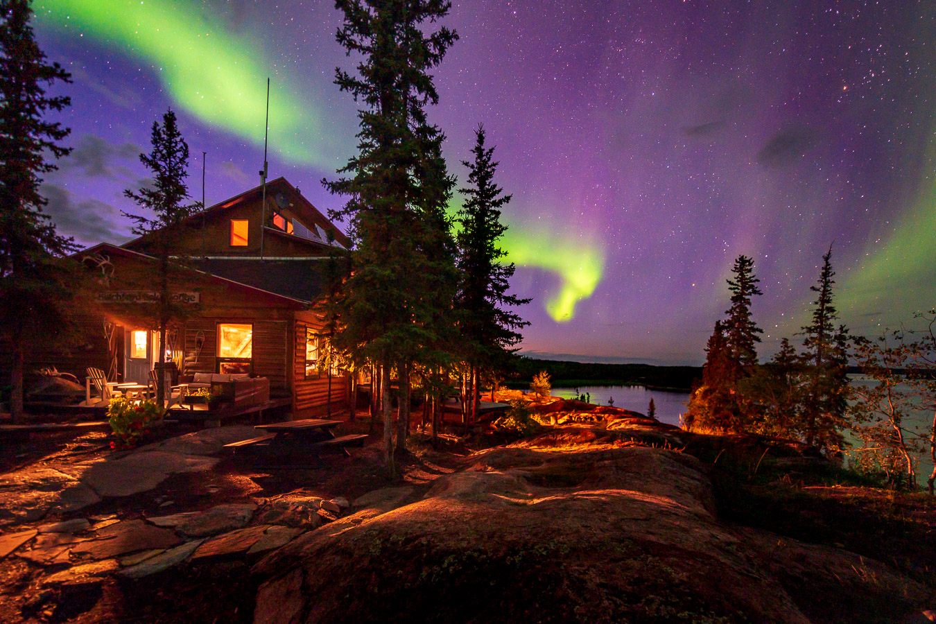 The aurora borealis is shining over a cabin in the woods