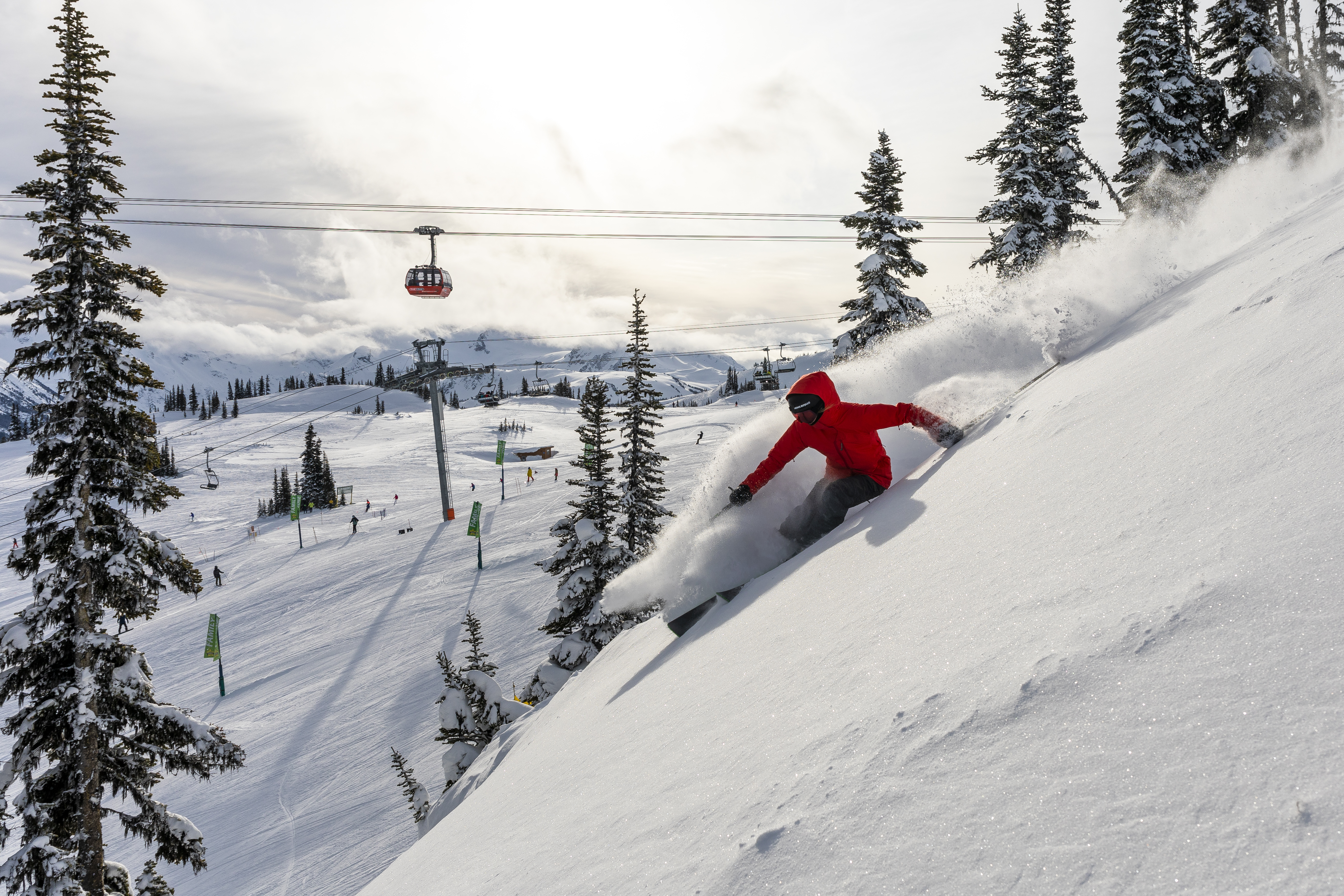A person in a red jacket skiing down Whistler mountain with gondola in the distance