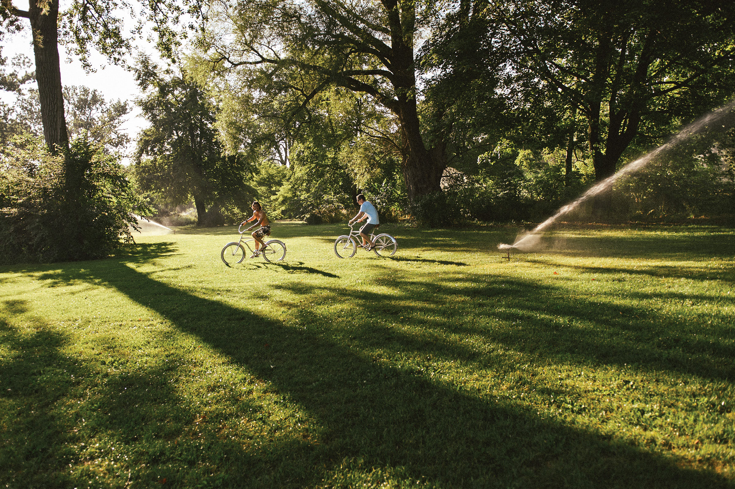 A couple bike over the grass in lush area in the Toronto Islands