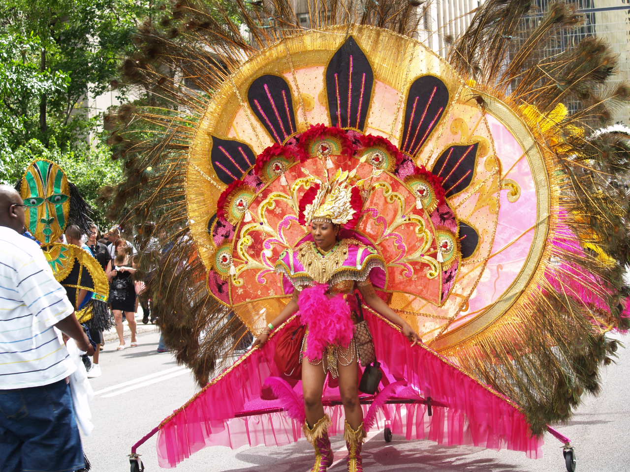 A woman in a pink and gold Caribbean carnival costume walks down the street