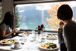 Two women enjoy a meal in VIA rail dining car while admiring the lake view out the window