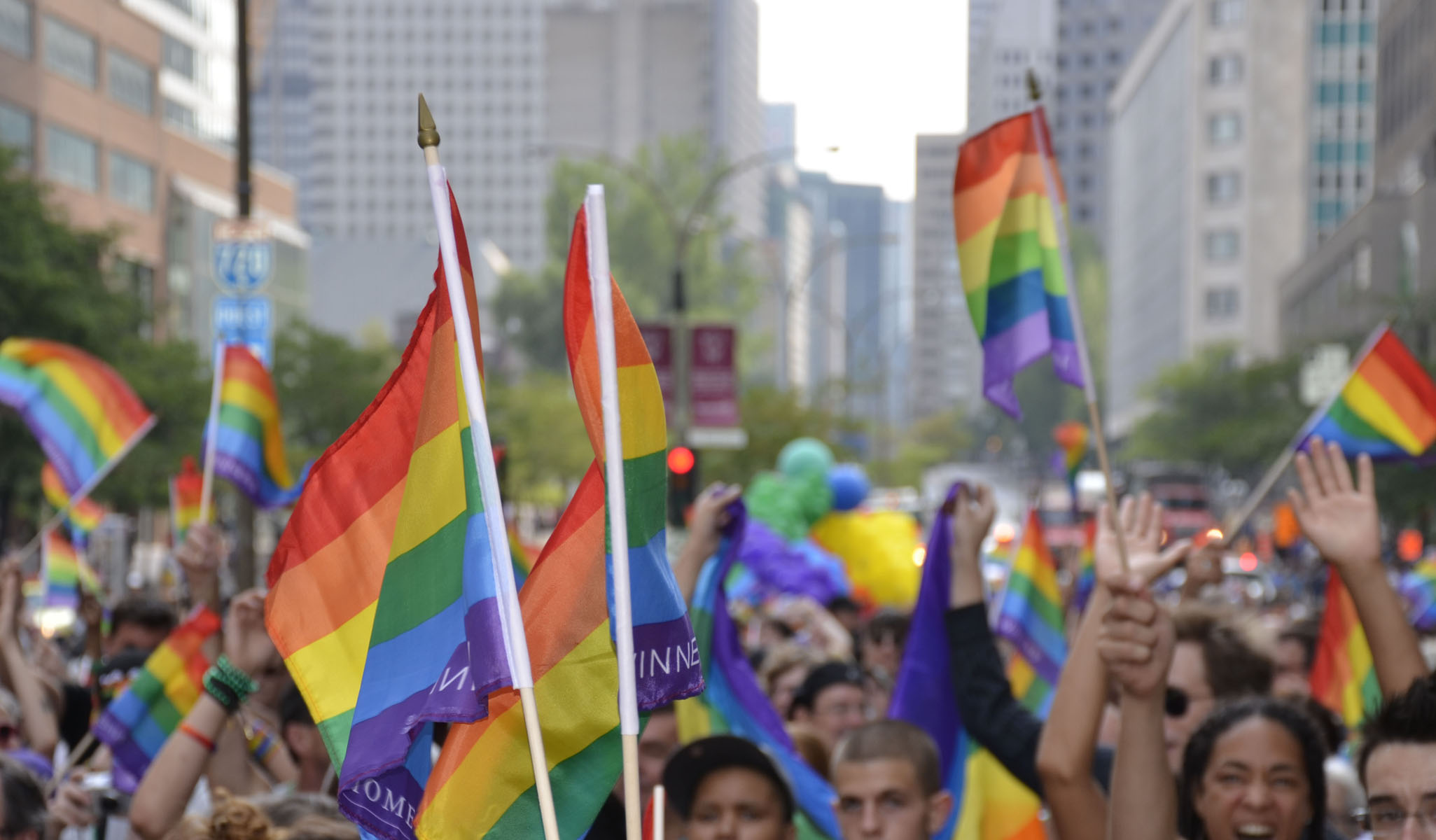 Crowd waves rainbow pride flags in a parade at Montreal Pride