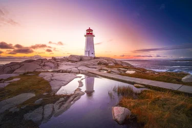 Sunset over Peggy's Cove lighthouse  with a reflection is seen in a pool of water gathered on the rocks.