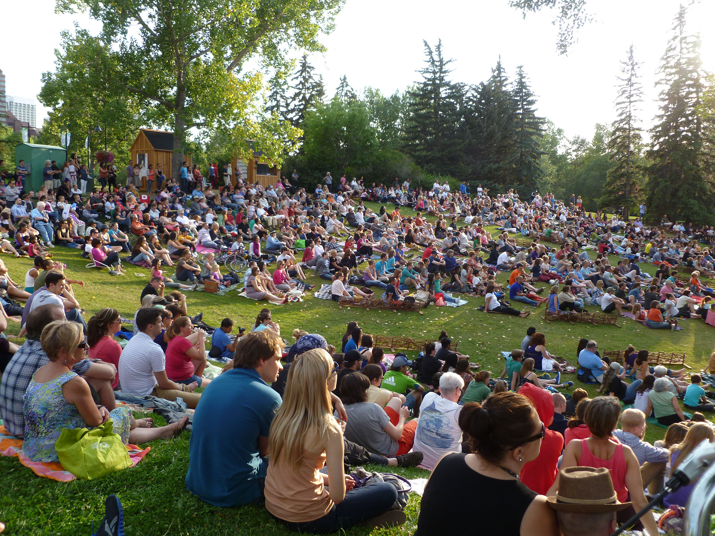 Crowd sitting on the grass watching an outdoor theatre show in Calgary