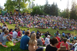 Crowd sitting on the grass watching an outdoor theatre show in Calgary