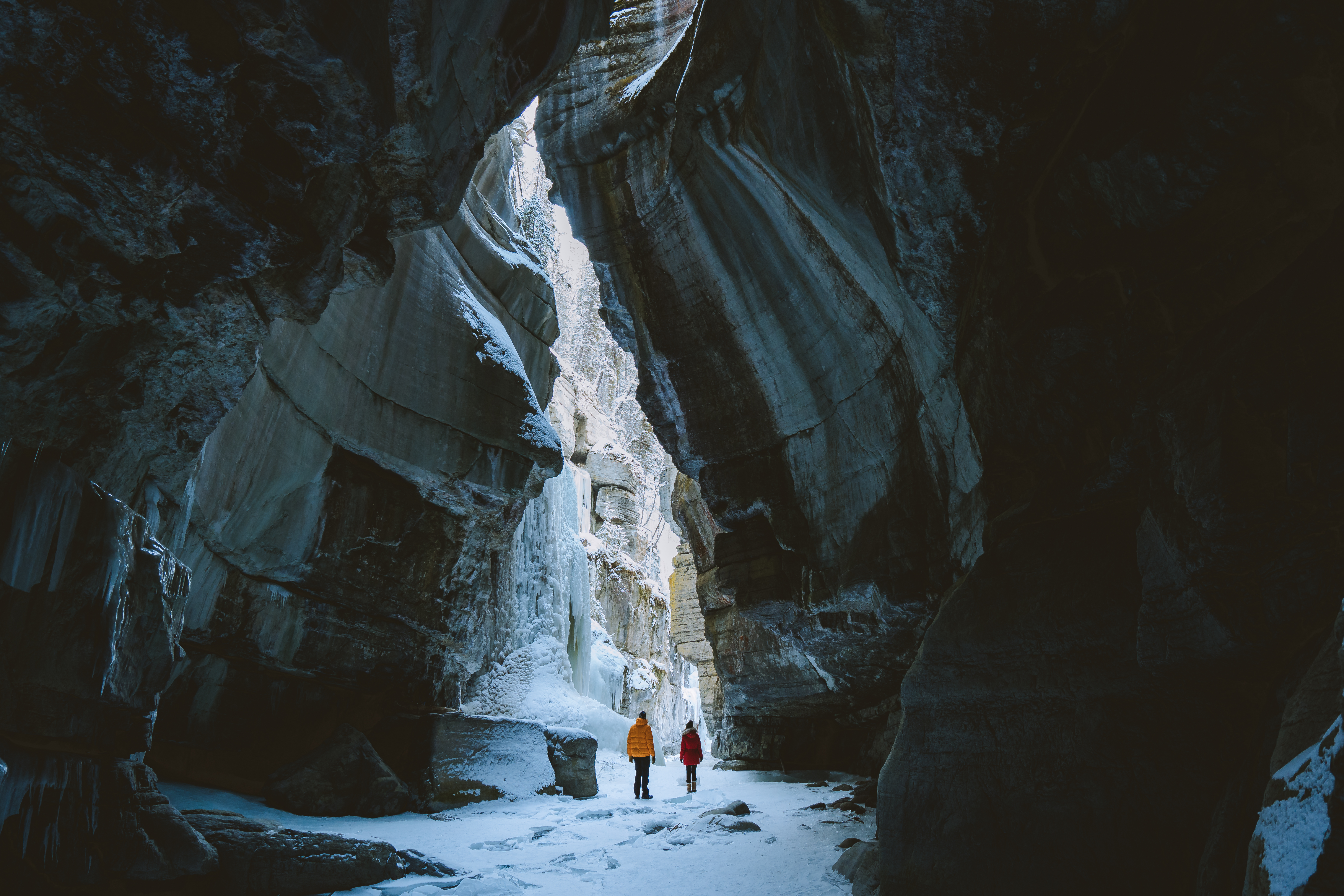 Two people exploring a canyon cave in the snow