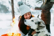 Woman gives hug to husky outside on a snowy winter day, by the fire