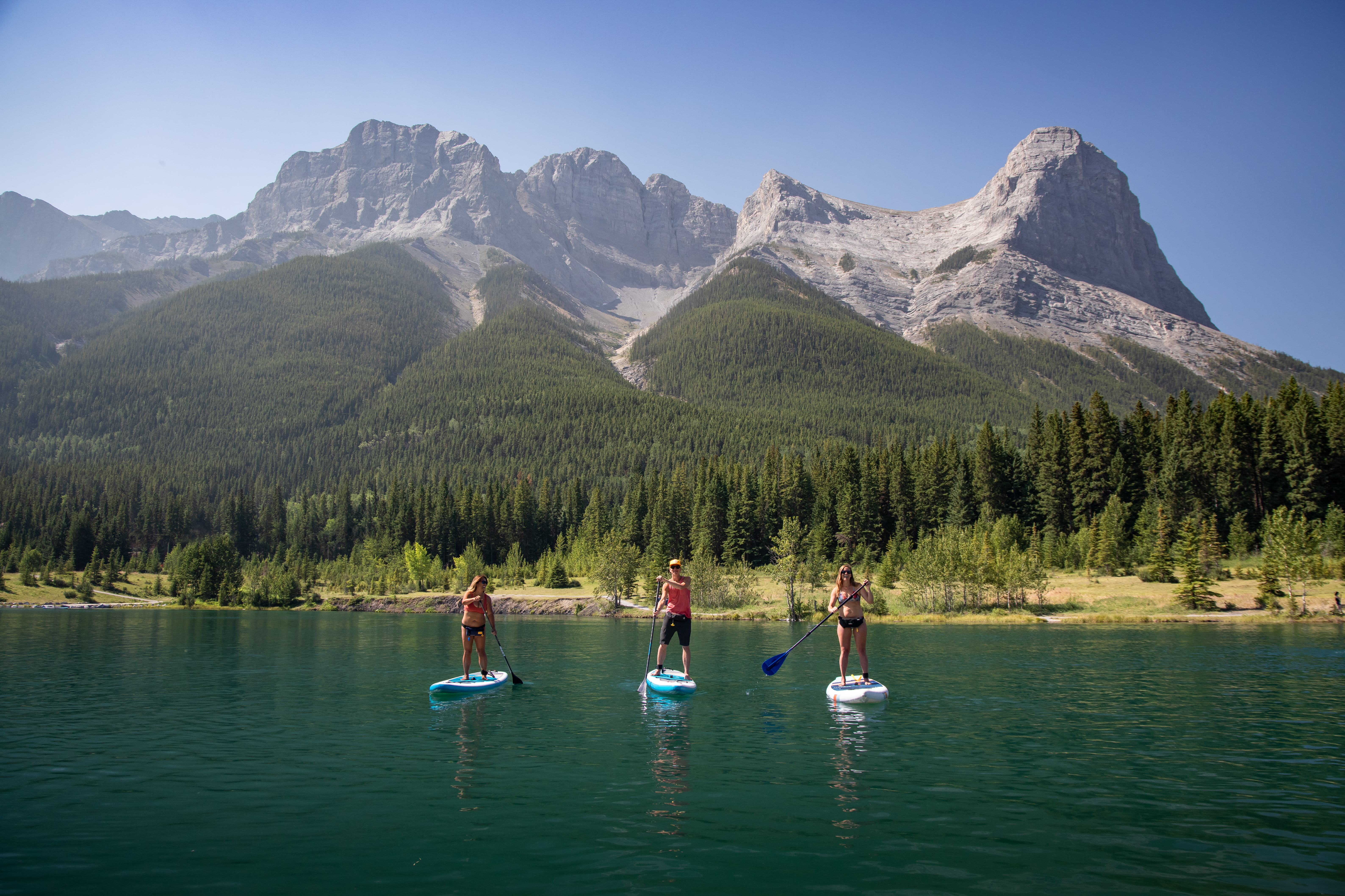 Three people paddleboarding on a Quarry Lake and mountains in the distance