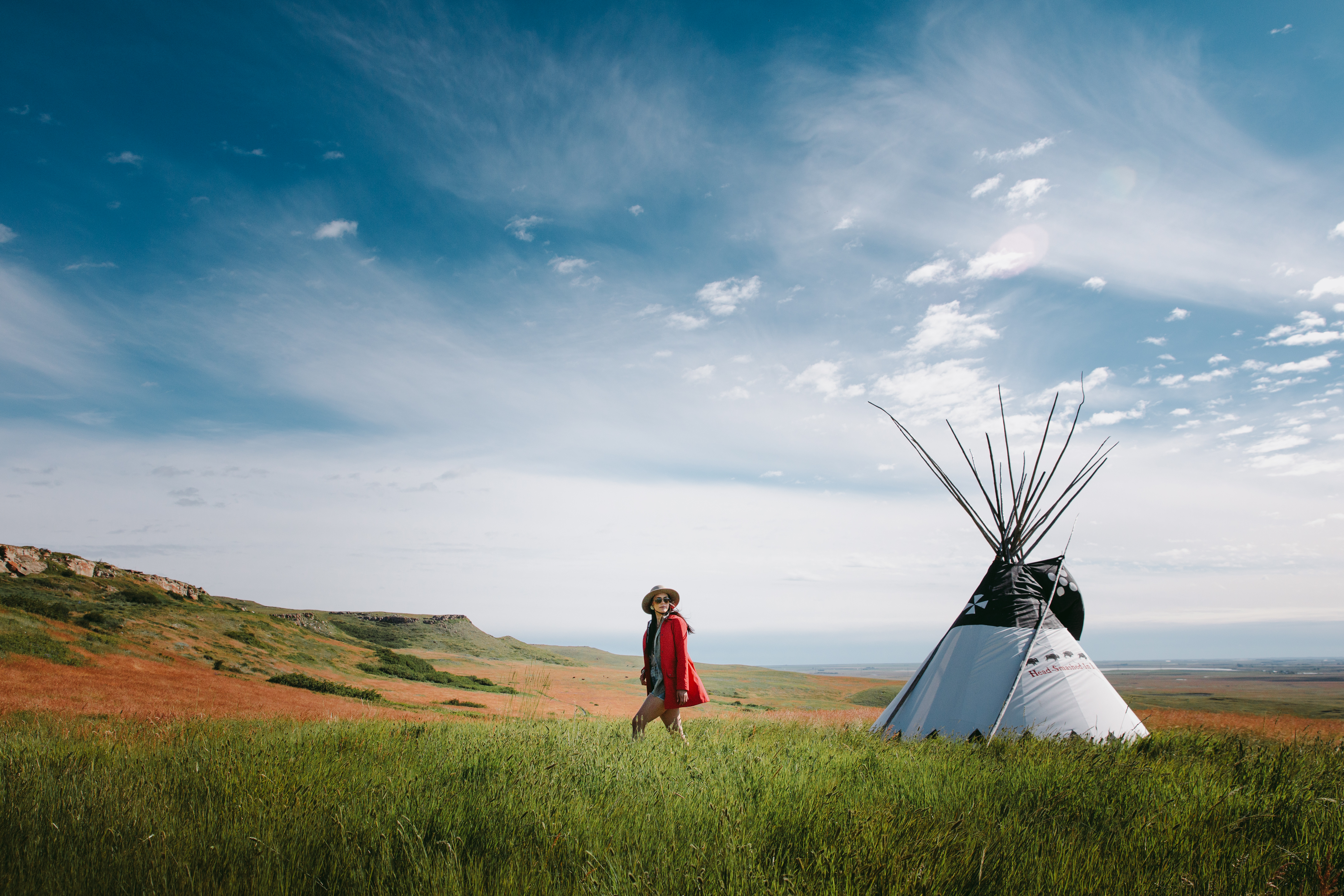 Person walking past a white tipi in a meadow at Head Smashed in Buffalo Jump