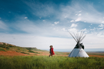 Person walking past a white tipi in a meadow at Head Smashed in Buffalo Jump