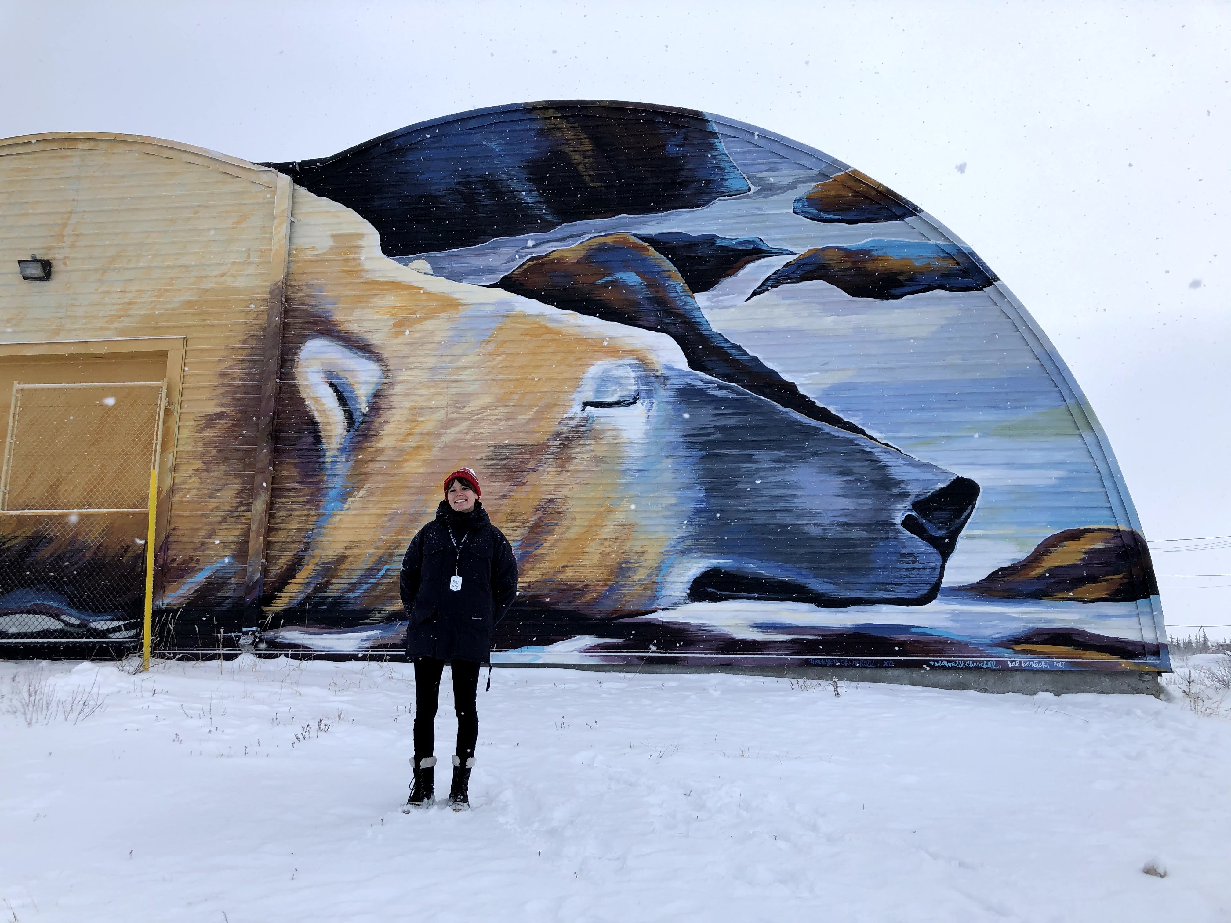 Haley Magwood stands in front of a polar bear mural in Churchill