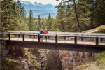 Two women stand on a bridge in Maligne Canyon with mountains behind