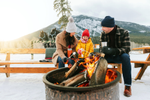 A family roasts marshmallows over fire while sitting on outdoor bench with a mountain in the background