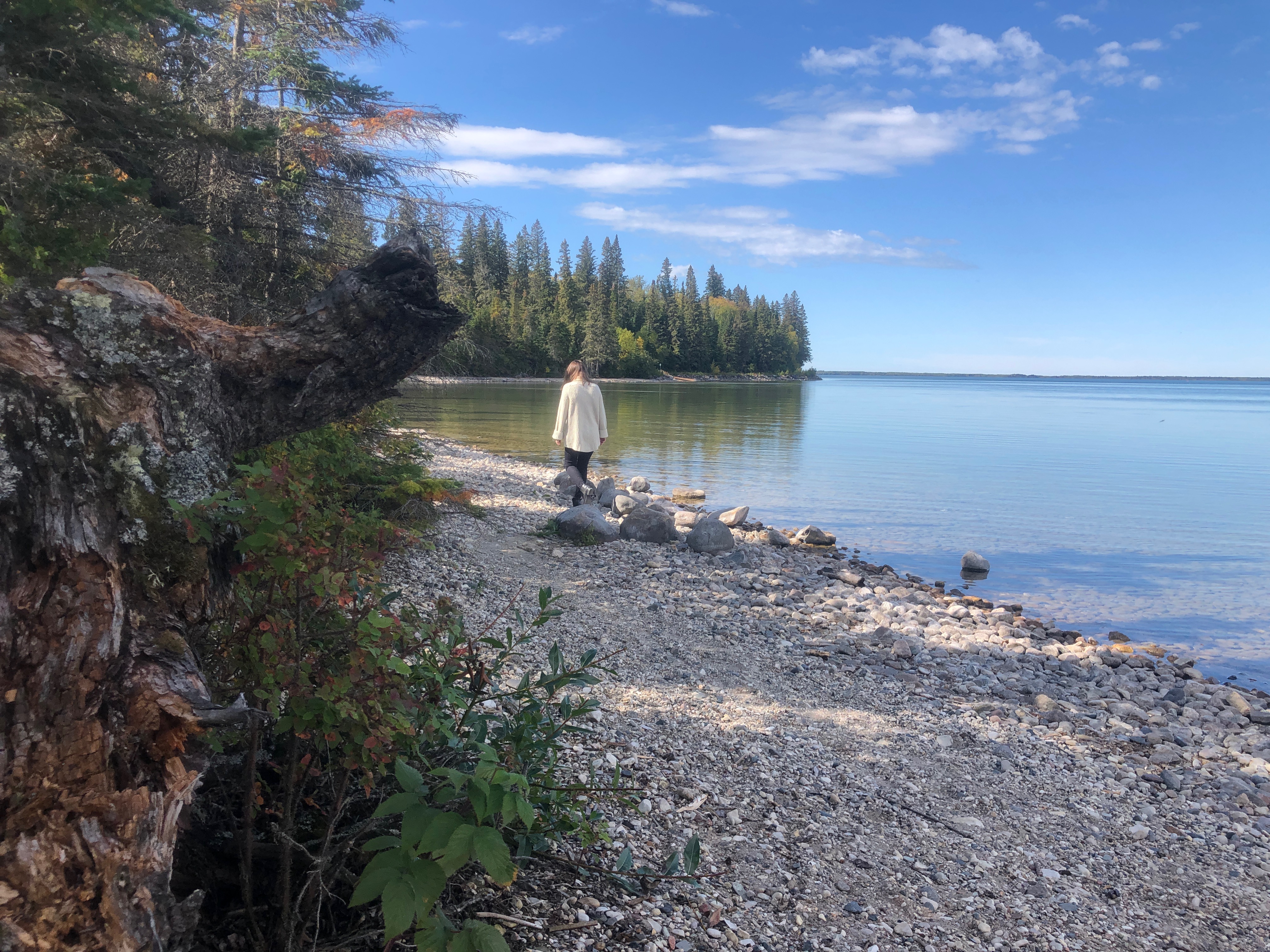 A person walks along the rocky beach next to Clear Lake, Manitoba