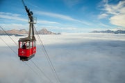 A small red tram car floats above the clouds in the Rocky Mountains
