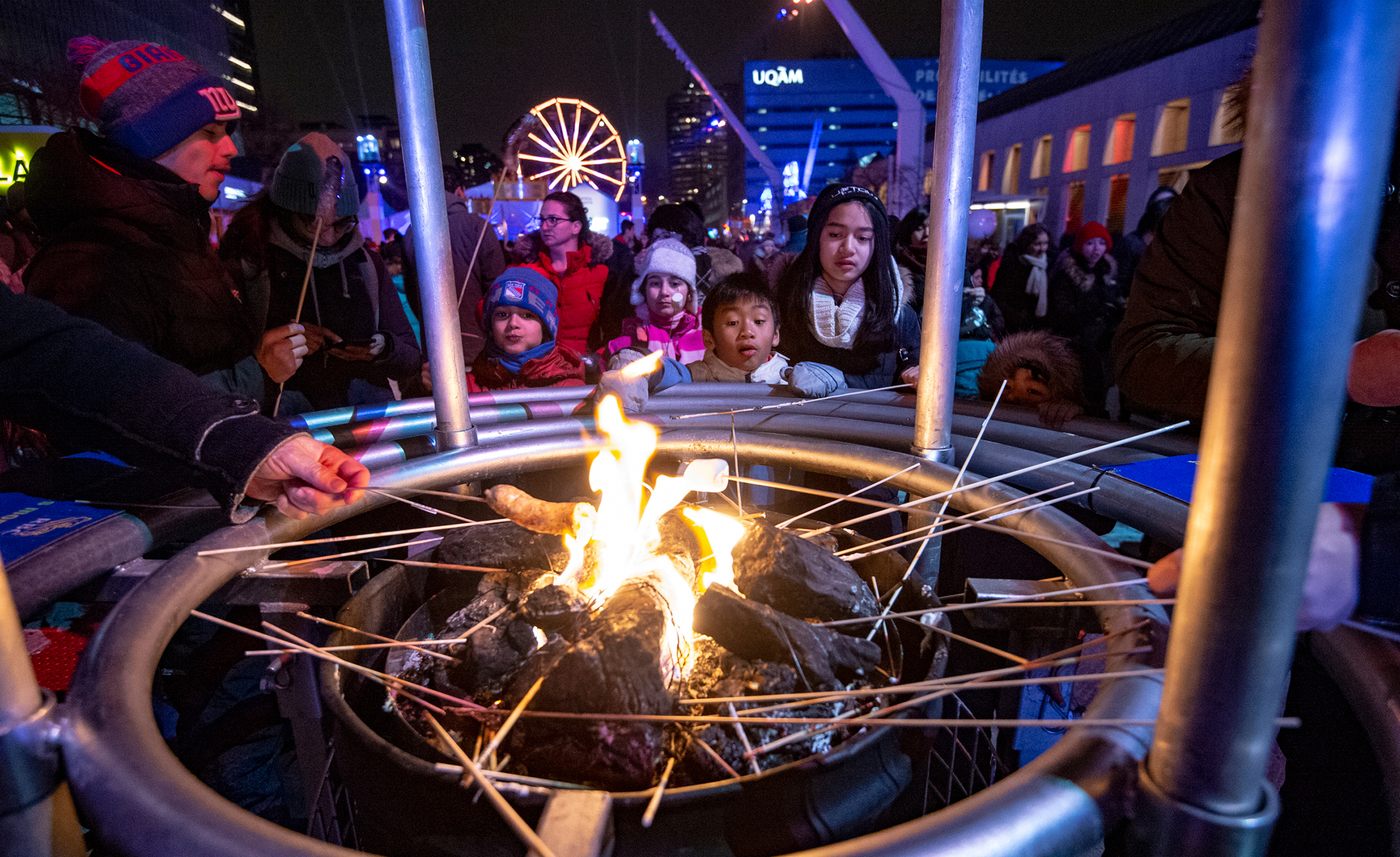 People holding sticks over a fire during an evening at a Montreal festival
