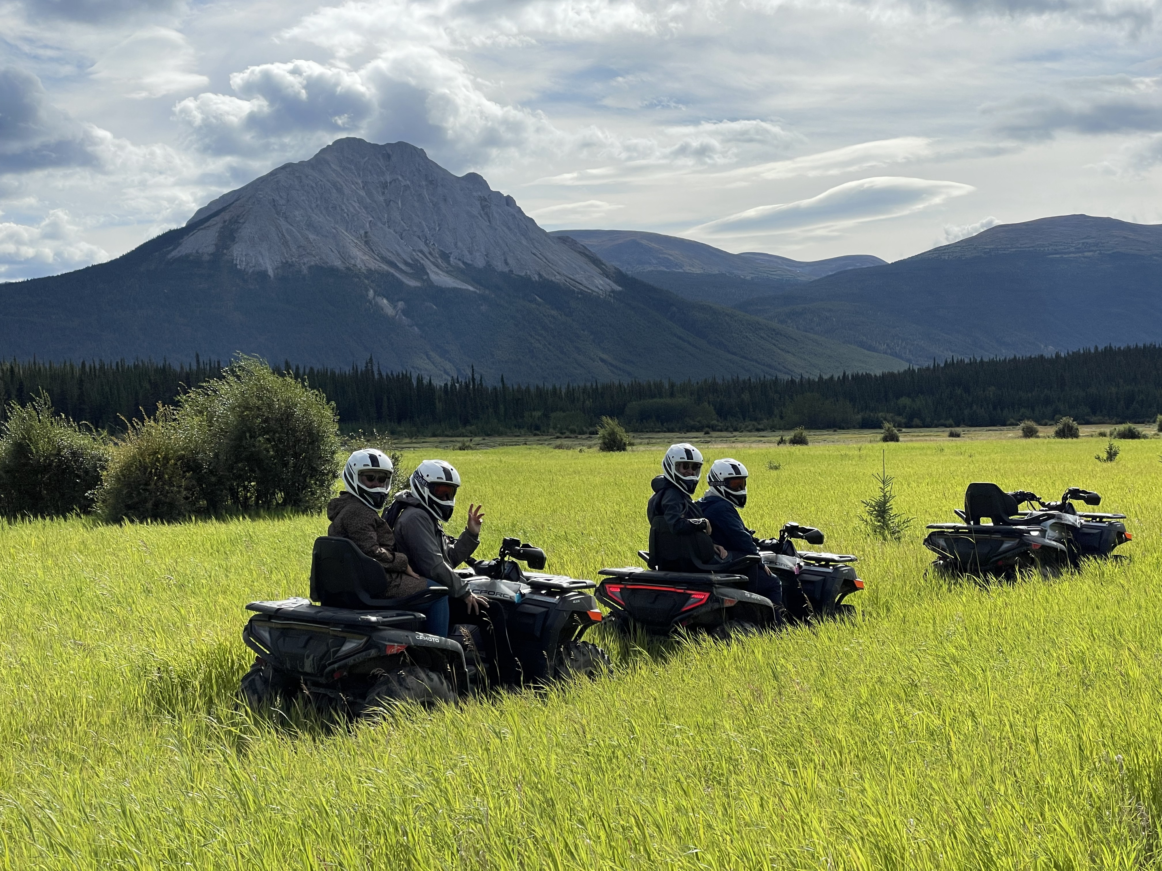 Small group on an ATV tour, going through green grassy field with mountains in the distance