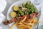 Serving of Souvlaki with meat skewer, French fries, lemon and dressed salad on a plate
