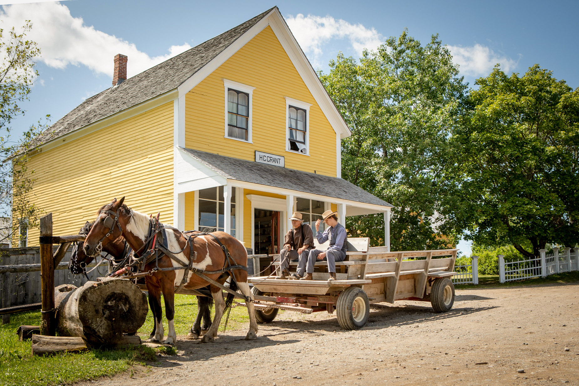 Two men in costume sit in wooden horse-drawn wagon in village as part of museum live adaptation depicting history of New Brunswick’s population