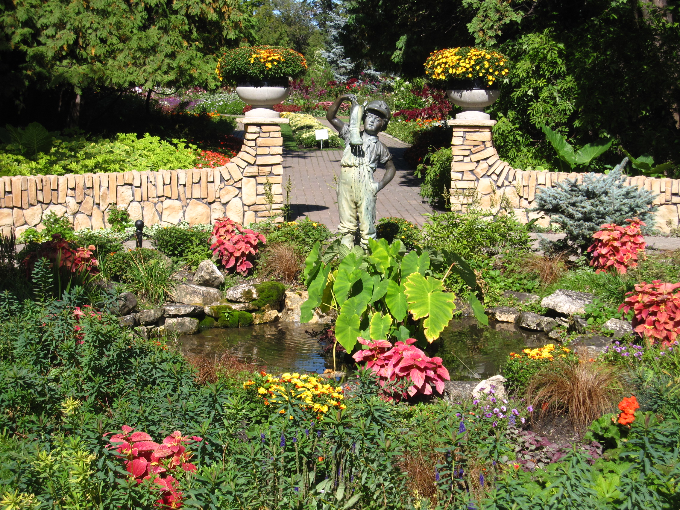 Sculpture of a boy with a boot, flowers and pond in a formal English-style garden