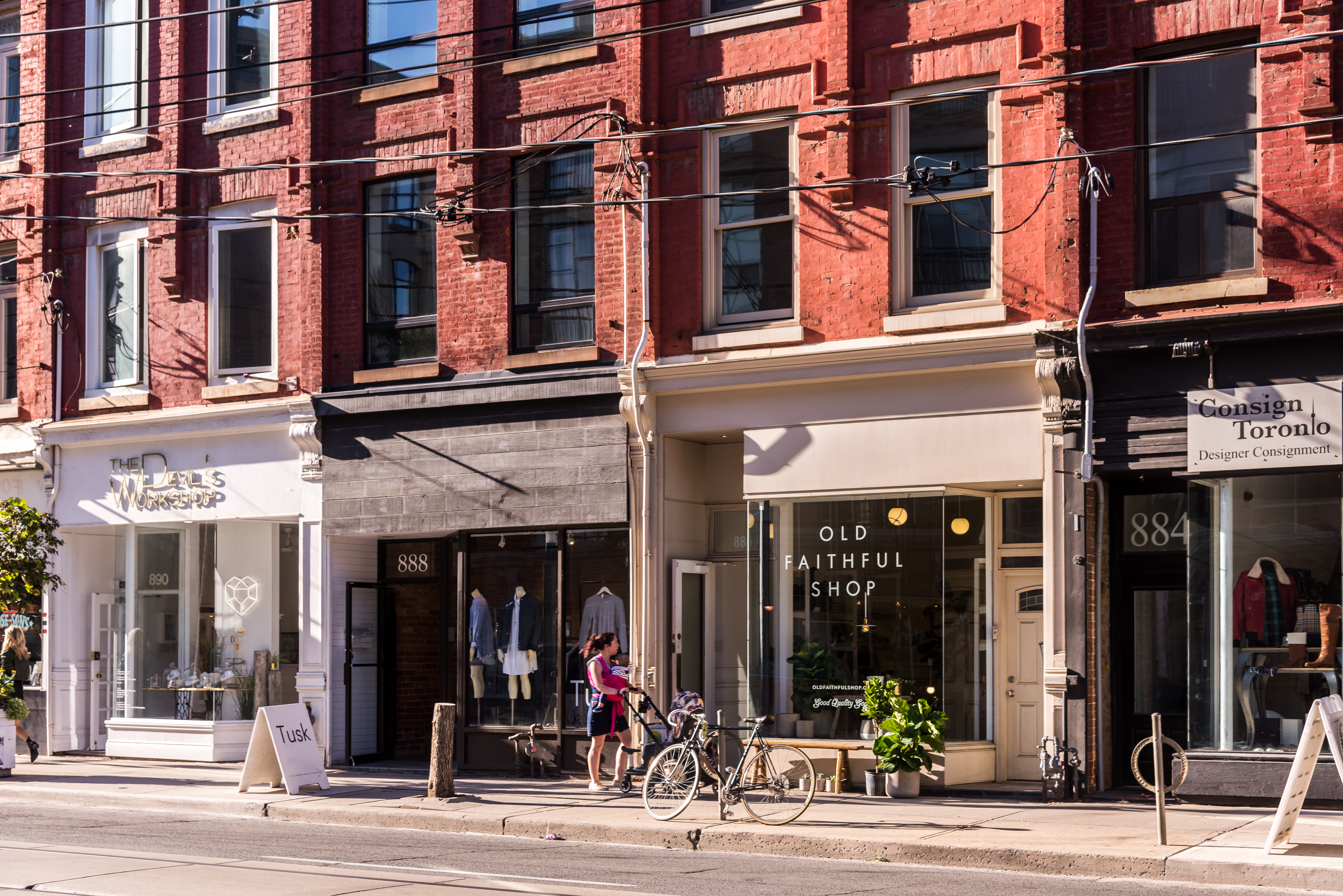 A person walks past boutique shops and red brick buildings on Queen Street West 