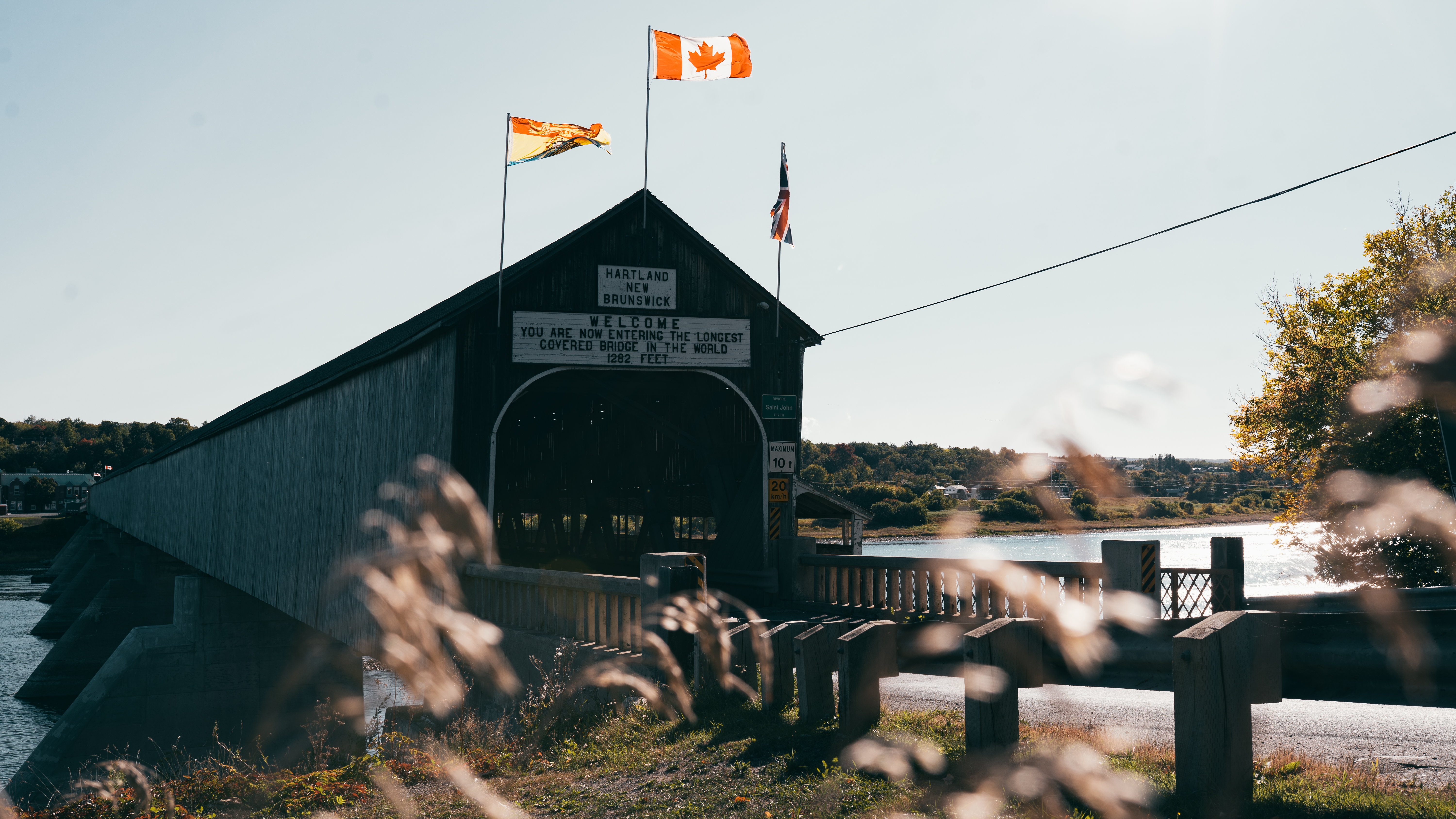 Covered wooden bridge with flags above entrance stretches across Saint John River