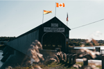 Covered timber-truss wooden bridge with flags above entrance stretches across Saint John River