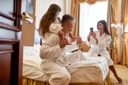 A family plays around on a hotel bed while wearing bathrobes