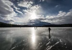 People playing hokey on a lake with mountains behind