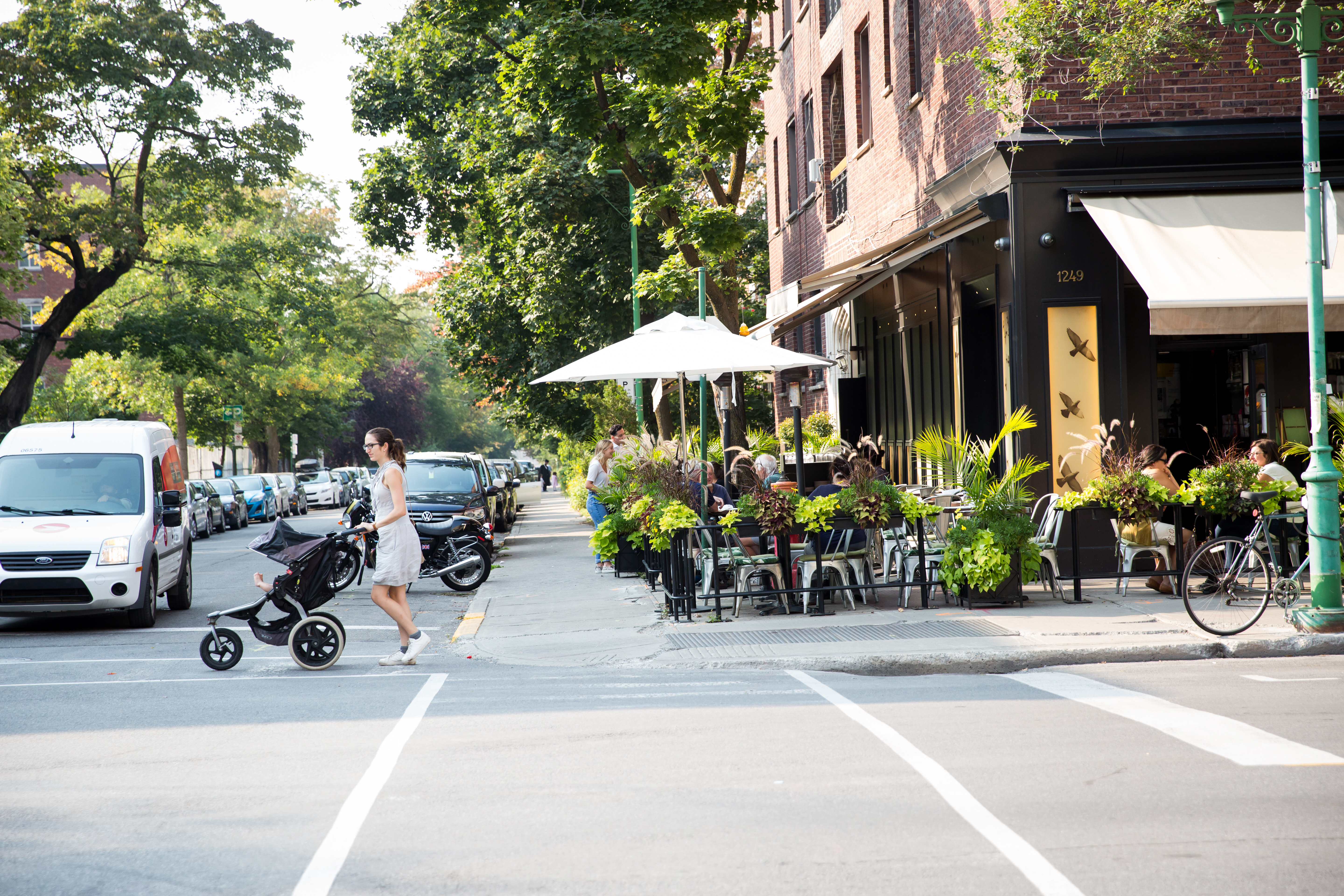 Pretty street corner with a cafe and patio seating, and a woman pushing a stroller across the road