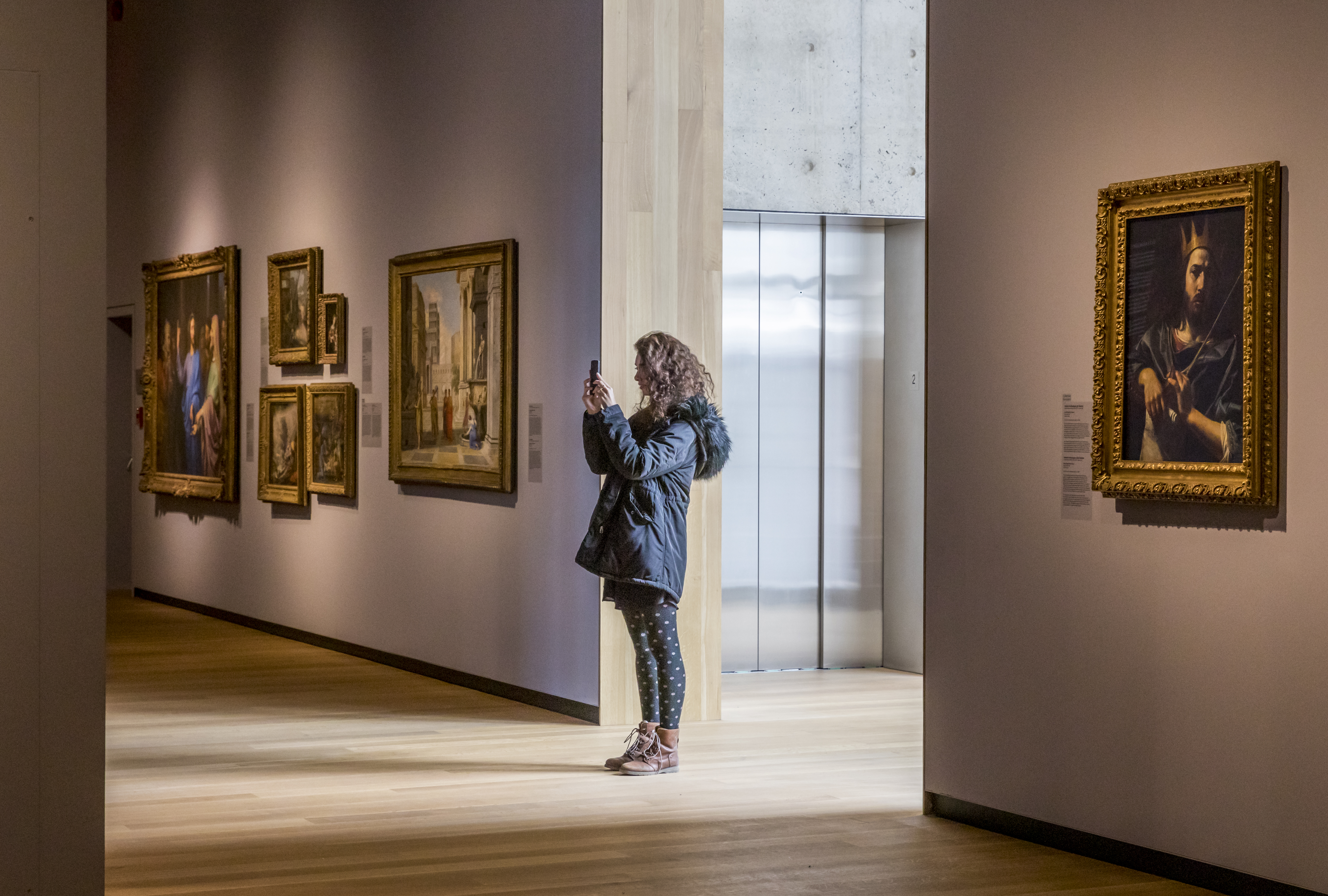 A woman standing in an art gallery taking a photo on her phone