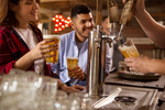 A couple waits at a bar while holding beers