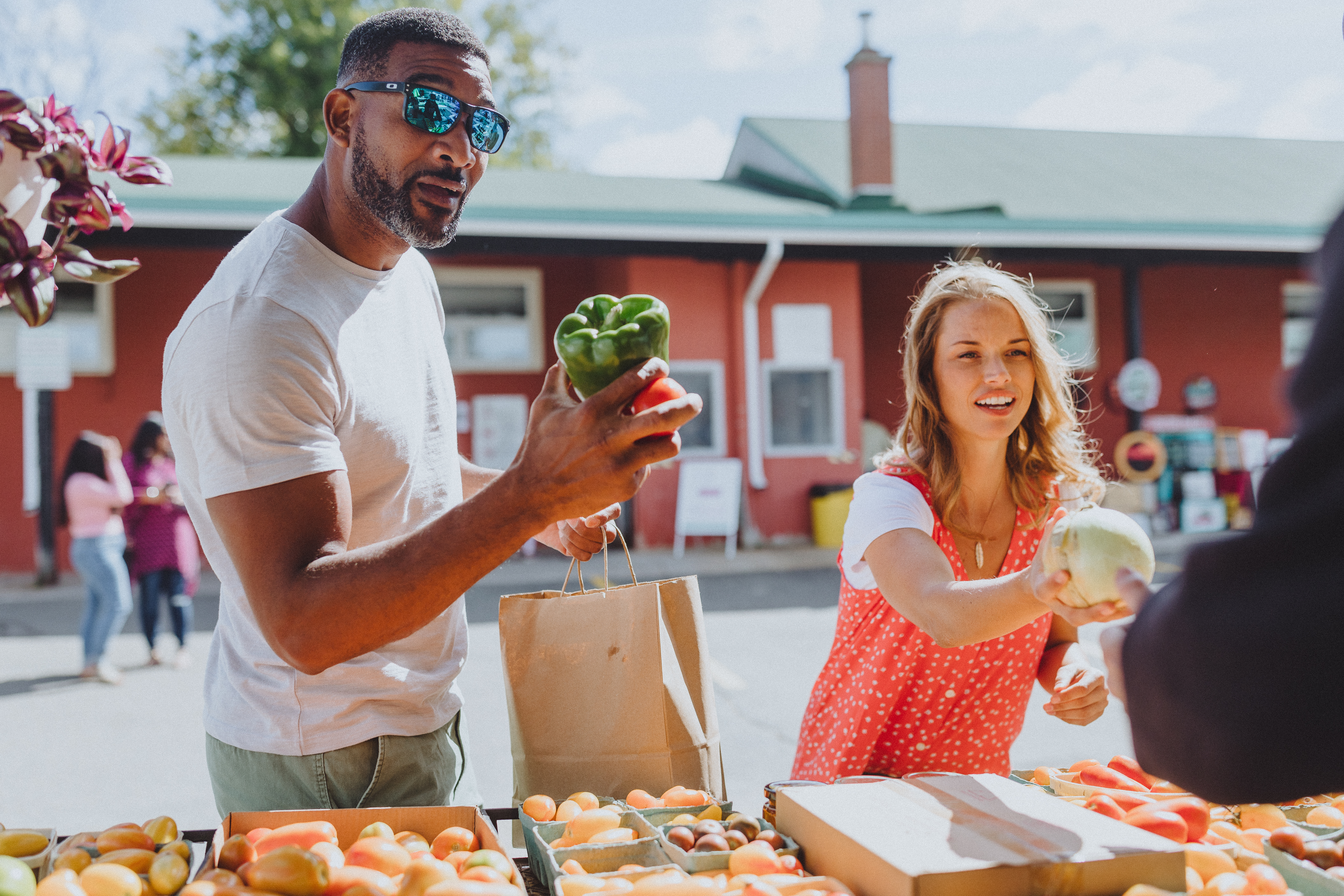 Cheerfu shoppers holding fresh produce converse with vendor at rustic Fredericton Boyce Farmers' Market