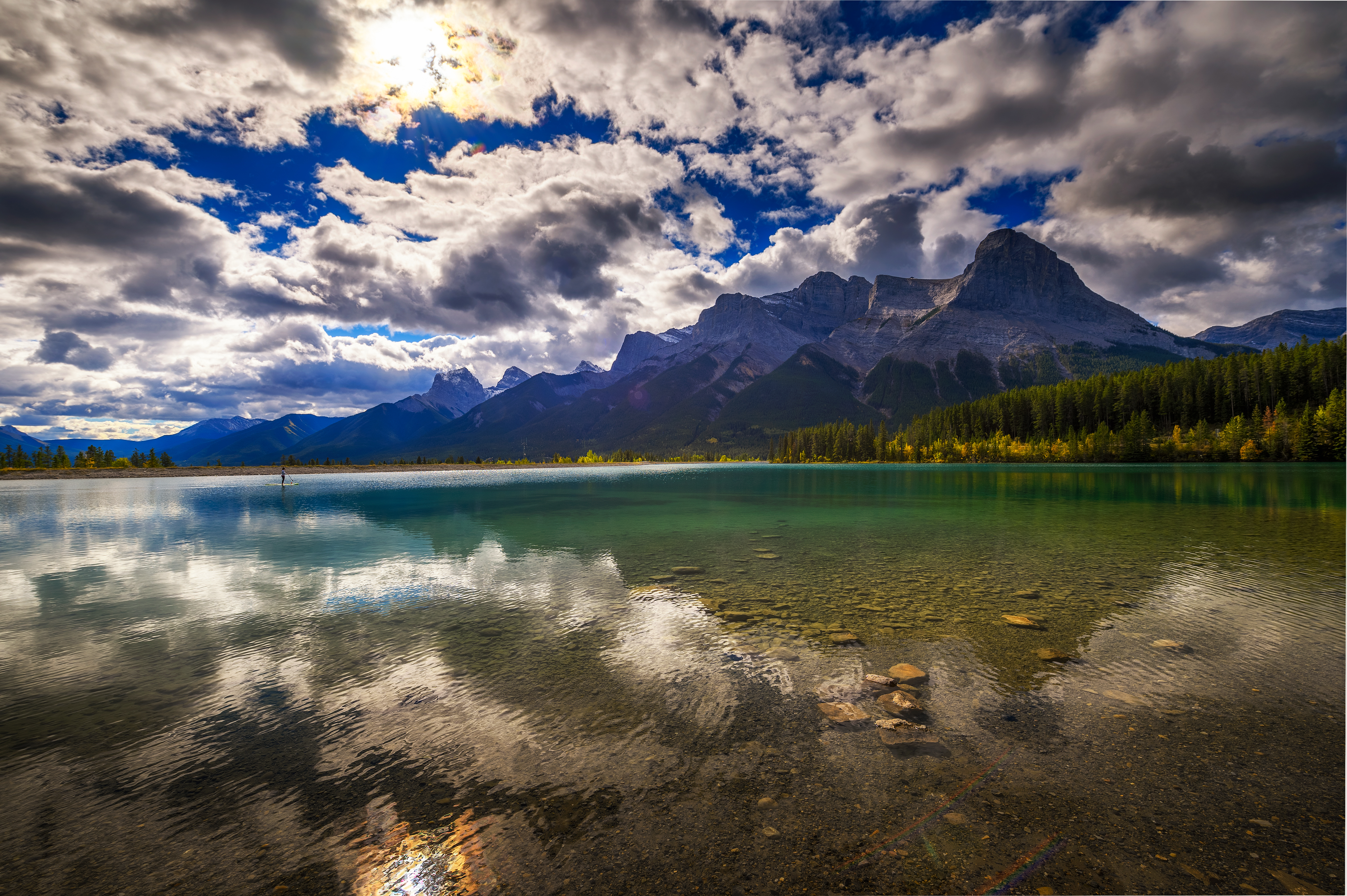 Woman paddles in clear turquoise Rundle Forebay Reservoir water in front of Three Sisters Mountain Range in Canmore