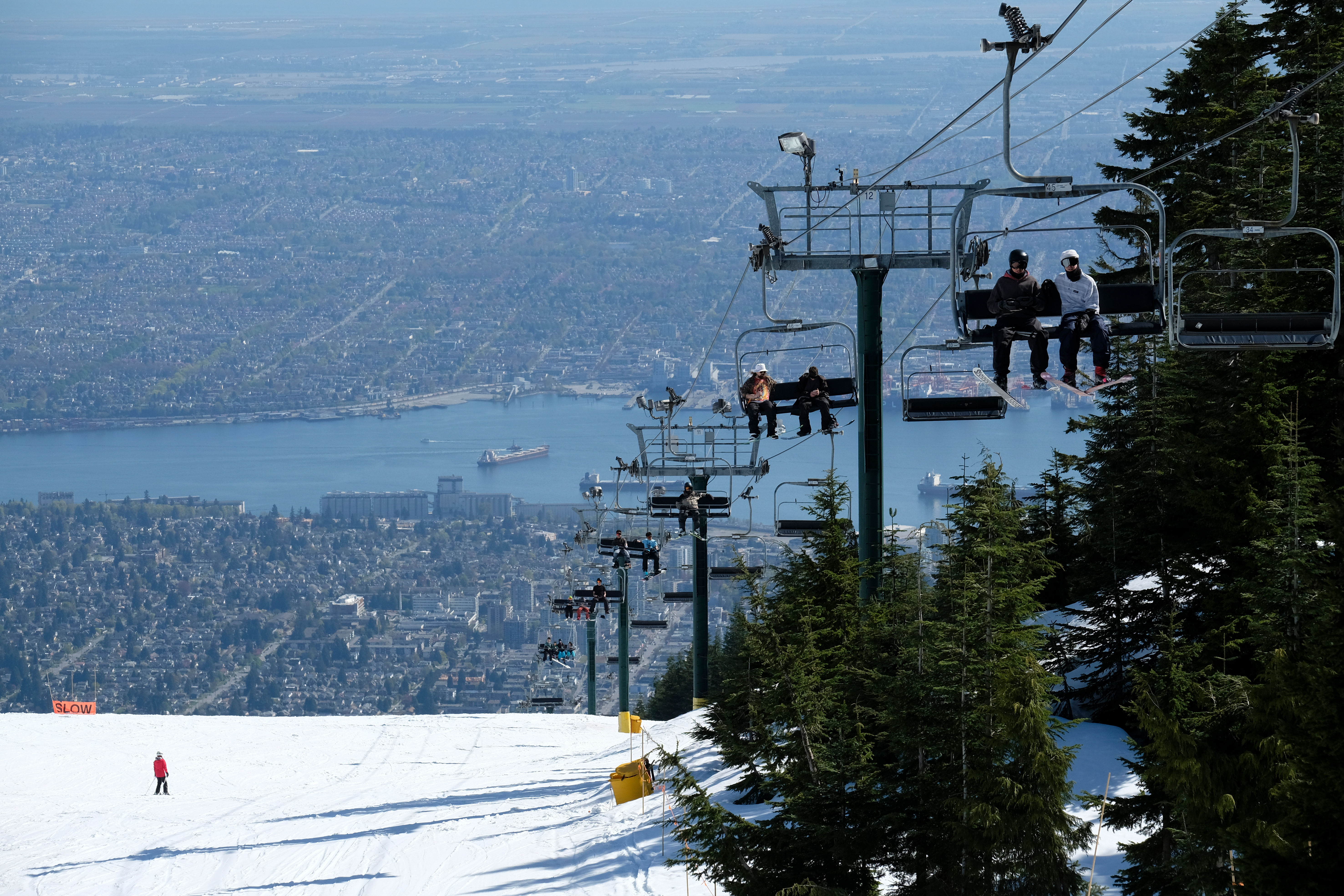 People sitting on a ski chair lift above the snow with Vancouver city and ocean in the distance