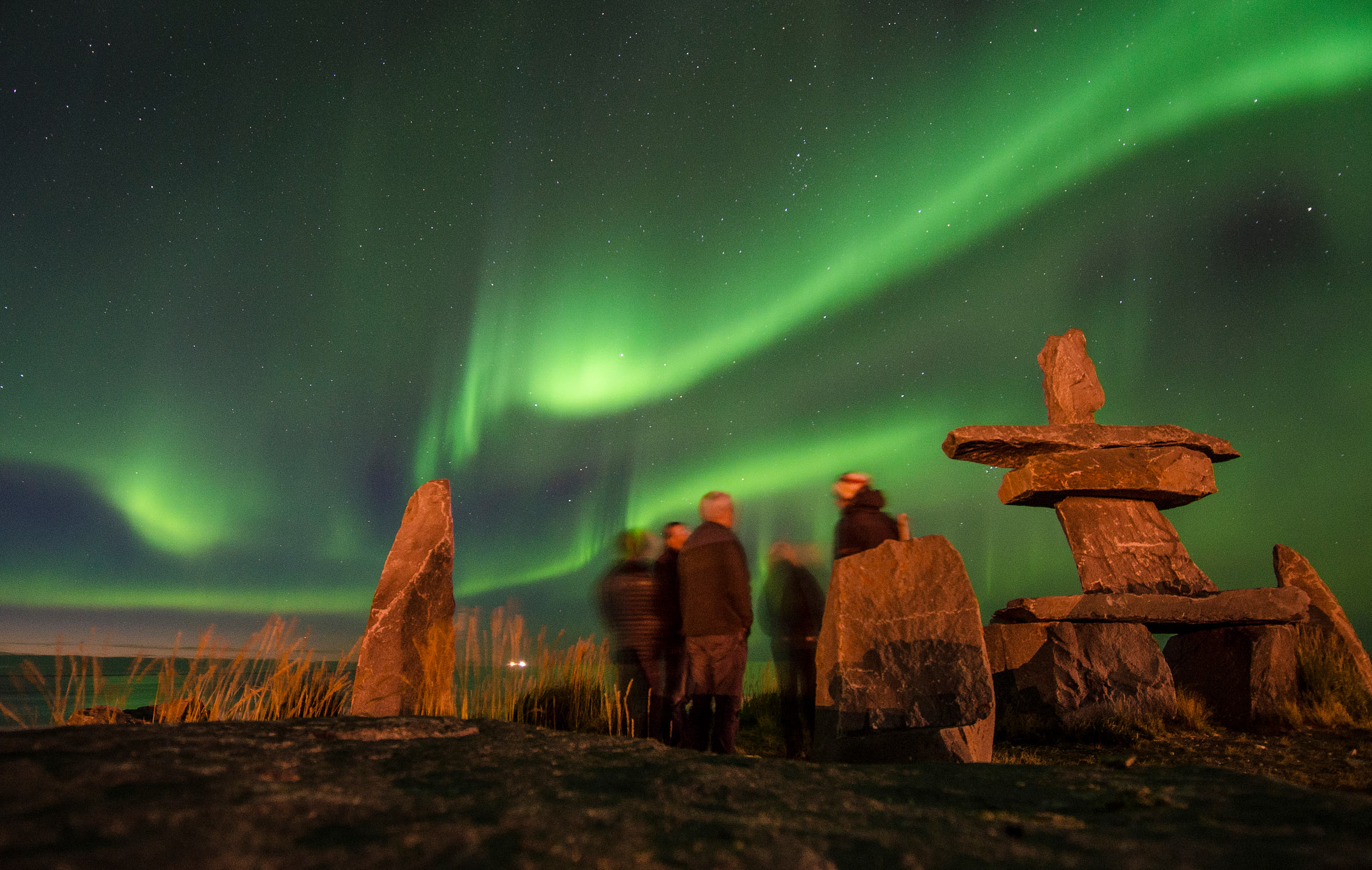 Green Northern Lights in the sky above a group of people next to an Inukshuk in Churchill