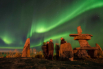 Group of people view the aurora borealis next to an Inukshuk in Churchill