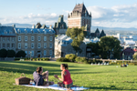 A couple having a picnic on a grassy hill in front of the Fairmont Chateau Frontenac