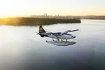 single otter seaplane flies over English Bay with views of Stanley Park and Vancouver skyline in background