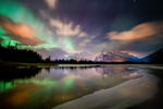 Colourful Northern Lights above a lake and snowy mountain range in the Rockies