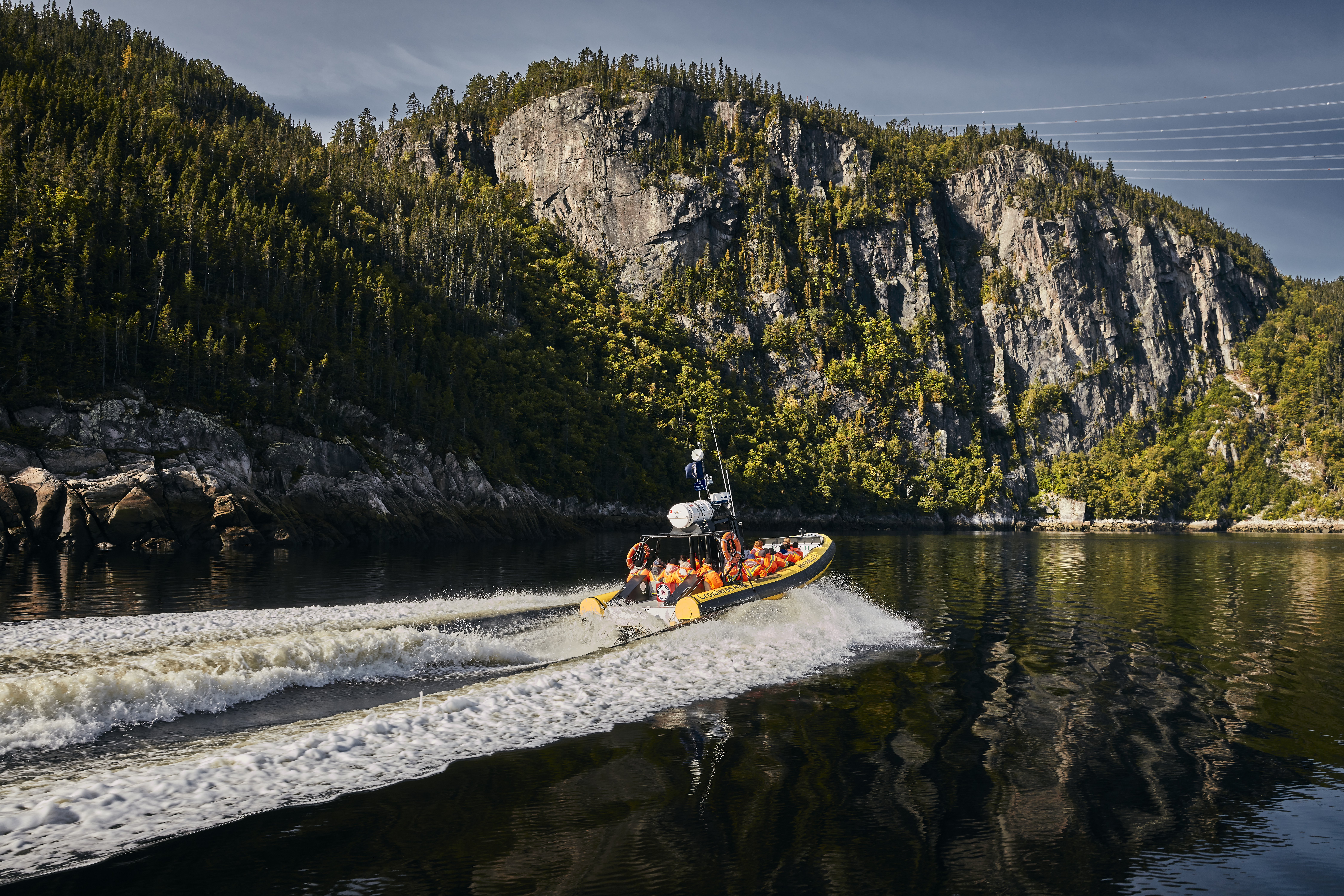 A yellow zodiac boat cruises past steep cliffs in the Saguenay Fjord