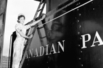 A woman in uniform stands on a ladder and washes a Canadian Pacific Rail Car in a dated black and white photo