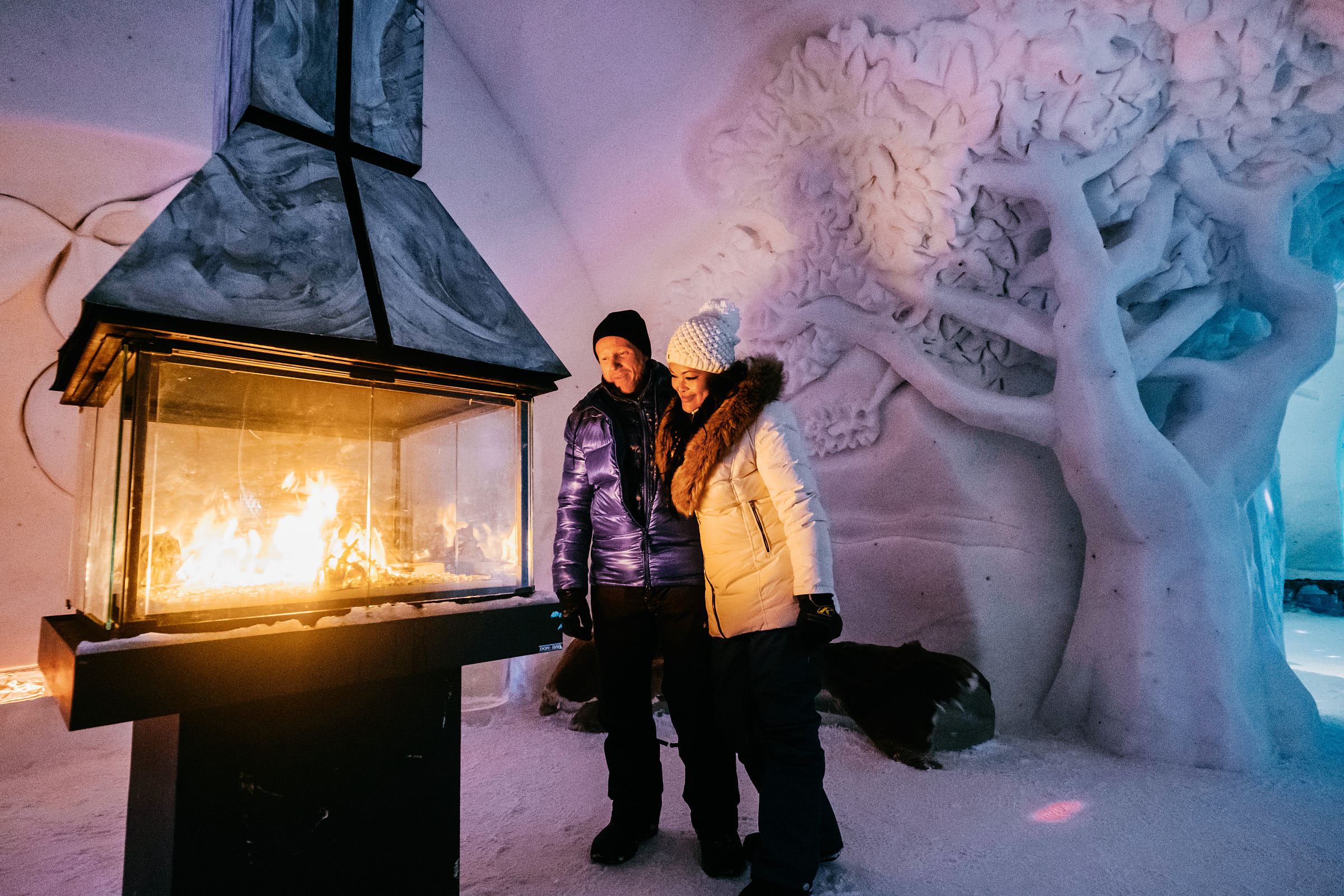 Couple standing next to fireplace in an ice hotel