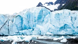 Man standing below massive glacier calving face