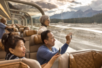 A couple take photos of the scenery while seated onboard Rocky Mountaineer GoldLeaf glass-dome train car