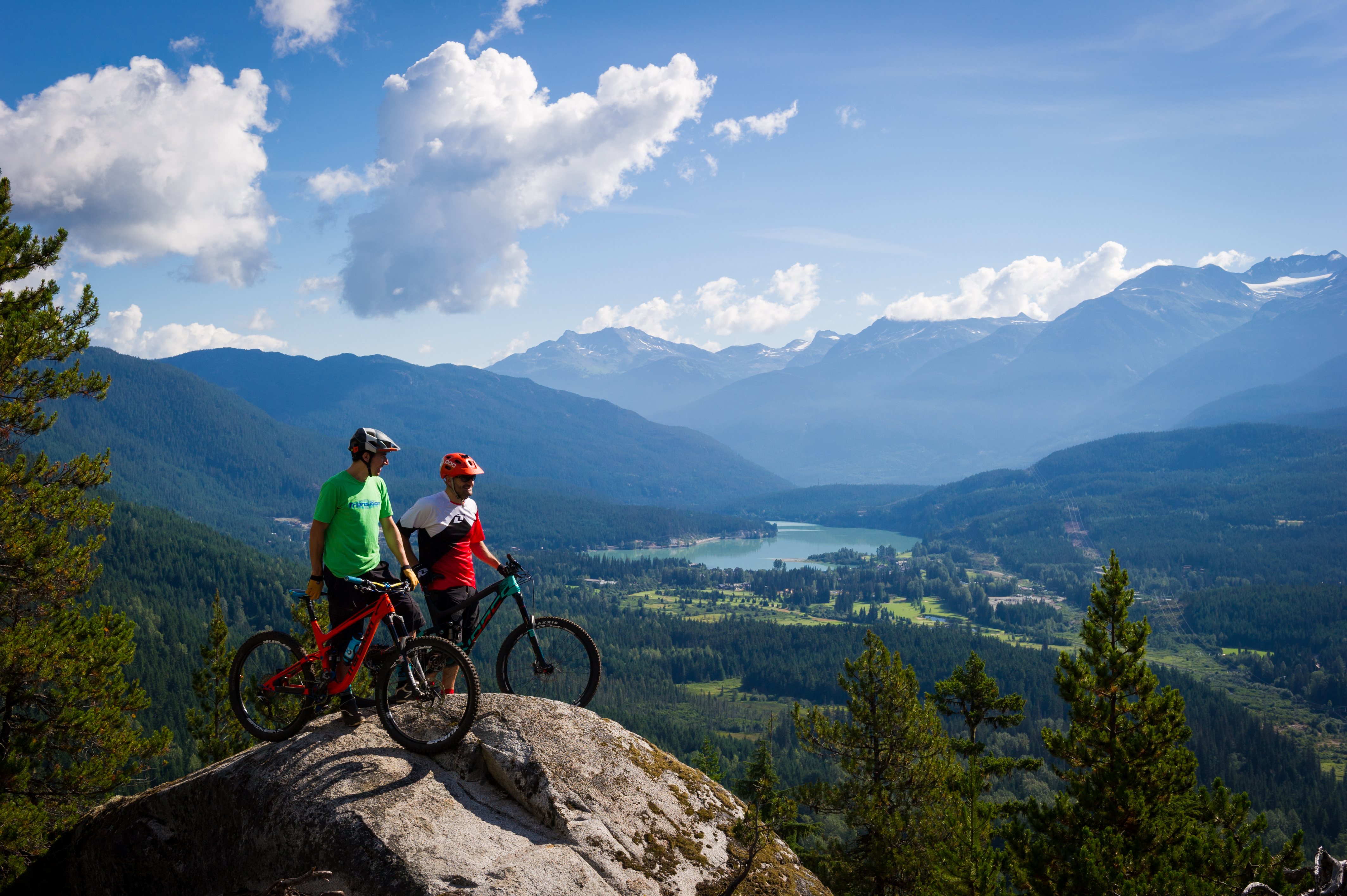 Two mountain bikers standing on a rock overlooking the mountains in Whistler