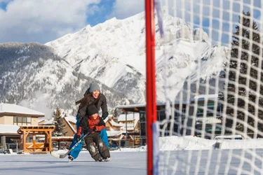 Boy and father play hockey on ice with mountains in the background