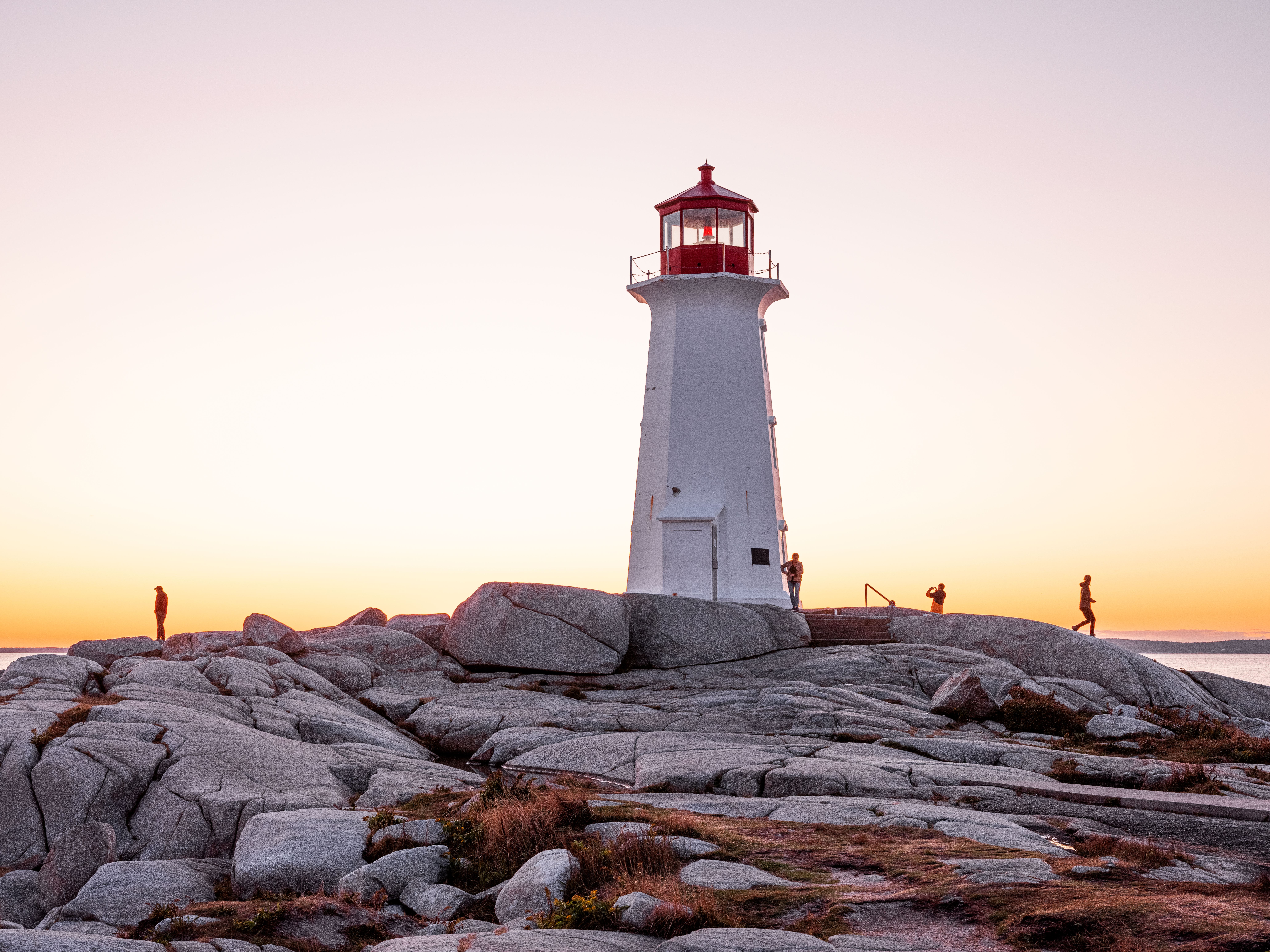 Silhouettes of visitors standing on rocks by coastal shore near lighthouse located in Peggy's Cove